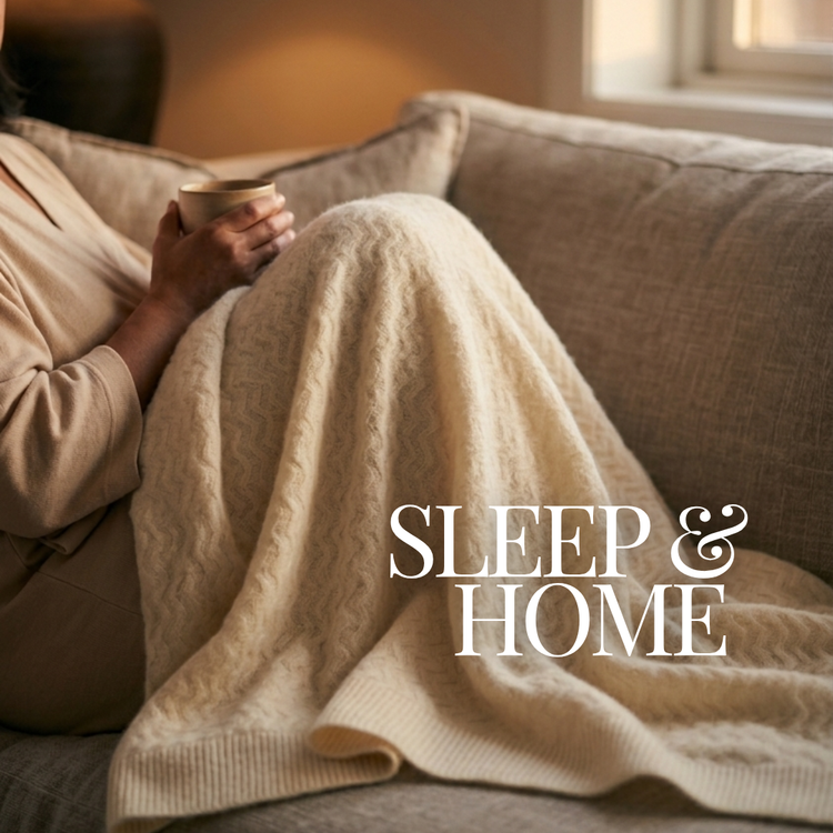 A cozy lifestyle scene showing a person reclining on a beige couch, wrapped in a cream cable-knit blanket and holding a mug. The text 'SLEEP & HOME' is overlaid on the front of the image.