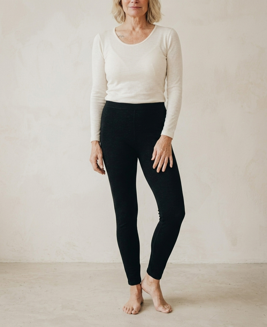 Woman wearing a white long-sleeve top and black leggings against a plain background